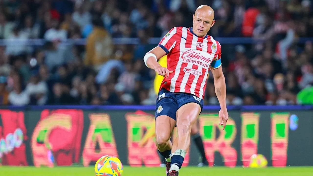 Chicharito runs with the ball in a red and white Chivas shirt